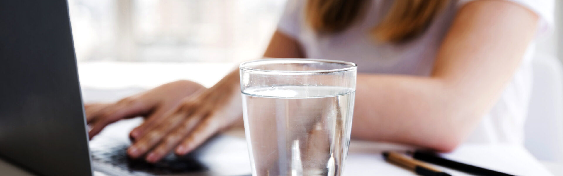 Frau arbeitet am Computer und ein Wasserglas steht neben ihr.