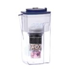 Transparente Wasserfilter-Kanne mit blauem Deckel, sichtbarer mehrschichtiger Filterkartusche und einem Fach für Kristalle am Boden.