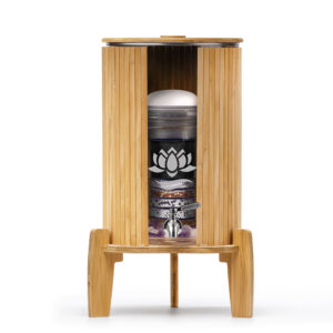 Ein Glas-Wasserspender mit sichtbarer Filterkartusche in einem Bambusgehäuse mit passendem Sockel, Deckel und Lichtschutz von Lotus Vita.