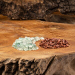 Zwei Haufen naturbelassener Wassersteine, hellgrüner Fluorit und rotbrauner Goldfluss, auf einer rustikalen Holzoberfläche.