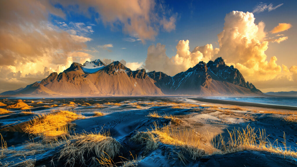 Die majestätischen Vestrahorn-Berge in Island, gespiegelt in einer von goldenem Gras gesäumten Wasserlandschaft bei Sonnenuntergang.