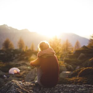 Eine Frau genießt bei Sonnenaufgang den Ausblick auf ein Bergpanorama, im Hintergrund ein Zelt.