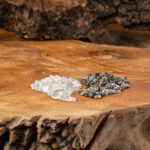 Zwei kleine Haufen getrommelter Edelsteine, heller Mondstein und dunkler Labradorit, liegen auf einer rustikalen Holzscheibe.