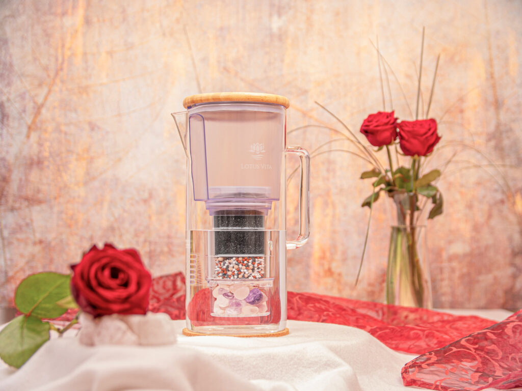 Eine Glas-Wasserfilterkanne mit Bambusdeckel in einer romantischen Szenerie mit roten Rosen.