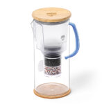 Eine Glas-Wasserkaraffe mit einem mehrstufigen Wasserfilter, einem Holzdeckel und einem blauen Griff, herausgebracht zum 20-jährigen Jubiläum von Lotus Vita.